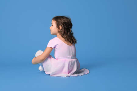 View from the back of a girl ballerina dressed in pink uniform looking away sitting on a blue background with space for textの写真素材