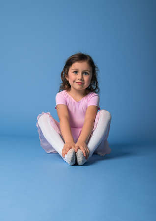 Portrait on a blue background of a cute ballerina in a pink dress stretching her body. Copy spaceの写真素材