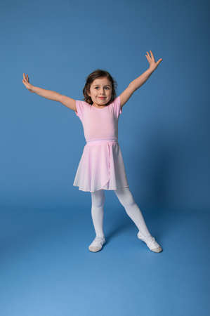 Full length portrait of a beautiful child ballerina performing ballet dancing isolated on blue background with copy spaceの写真素材
