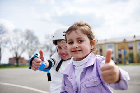 Face portrait of adorable children, boy in skateboard helmet and girl sitting next to each other and...