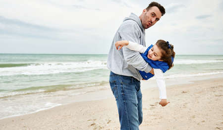 Handsome father holding his little cute daughter in his arms and playing together on the beach on a...