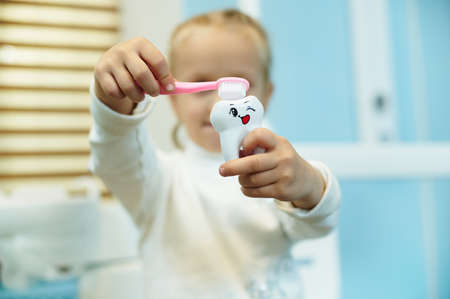 Adorable child brushing a white toy tooth with a toothbrush in the dental office. Oral care concept and teaching a child how to properly brush teeth to prevent decay of baby teethの写真素材