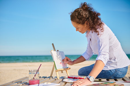Mature female painter enjoying painting on canvas outdoors on the sea background.の写真素材
