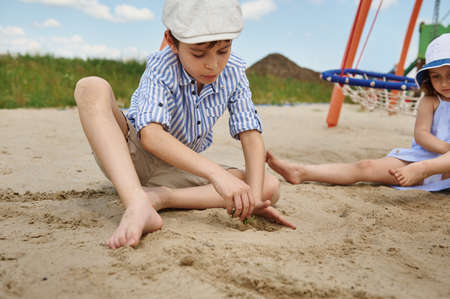 Cute schoolboy playing on the sandy playground , planting a green sprout in the sand. Playing outdoors, summer vacations concepts. Summer campの写真素材