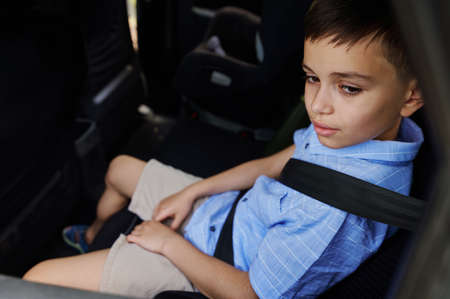 A teenage boy wearing seat belts travels by car in a protective child booster car seat. Traveling safely with children. Safe movement of children in the carの写真素材