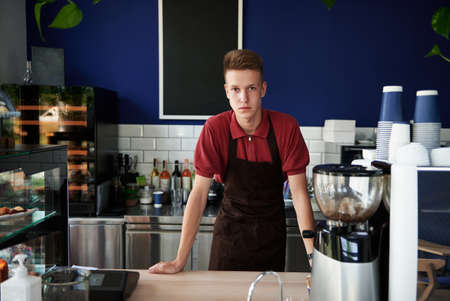 Professional portrait of young trained barista behind a bar counter in cafeteria. Small business, food and drink business conceptsの写真素材