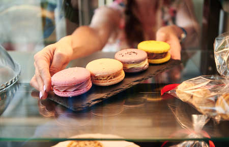 Close-up of a seller taking colorful macarons from a showcase in pastry storeの写真素材