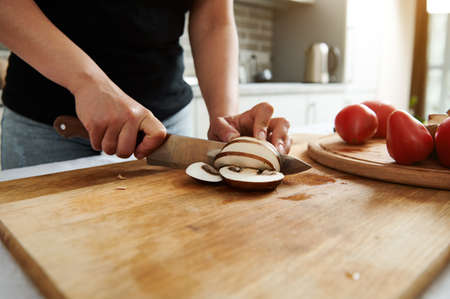Close-up of chef or housewife hands while chopping mushrooms on a wooden kitchen board