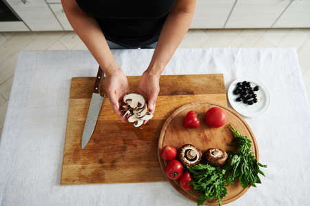High angle view of sliced mushroom in female chef hands. Ingredients for pizza filling on a wooden board in the home kitchenの写真素材