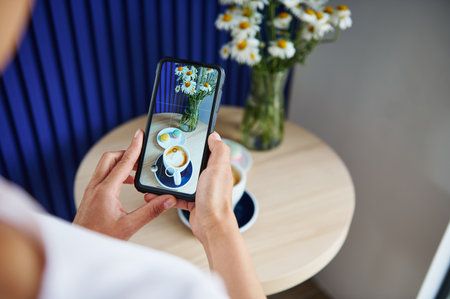 Unrecognizable woman taking a food photography of served table with macarons and cup of coffee latte...