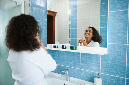 Rear view of beautiful African American woman in white waffle robe smiling cute looking at her mirror reflectionの写真素材