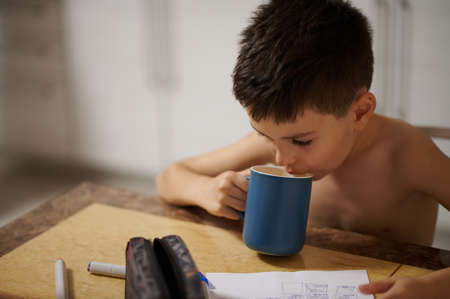 Cute boy sitting at table and drinking hot drink
