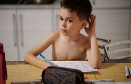 A drawing boy looks thoughtfully aside sits at the table in the kitchen