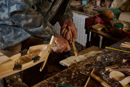 Carpenter using instruments to cut part of wood material to make wooden model of sailboat. Craftsman...