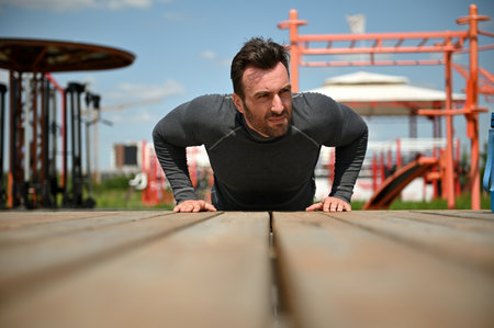 Sporty young Caucasian man doing push-ups on wooden surface exercising outdoors on sports ground...