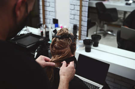 Rear view of a hairdresser combing hair of a business woman focused on remotely work, texting on...