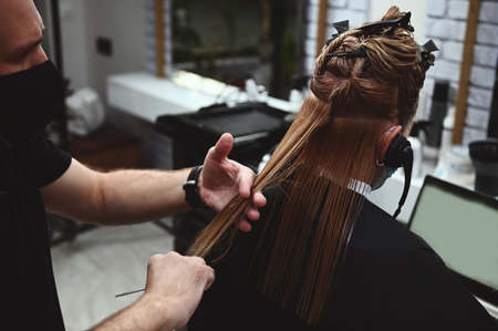 A hairdresser cuts the hair of a business woman who communicates with headphones on a laptopの写真素材