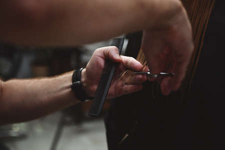 Close-up of a hairdresser holding a hairdresser scissors and a comb and cutting woman's hair at beauty salonの写真素材