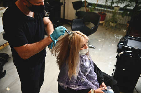 Side view of a salon client wearing a medical protective mask getting ready for coloring and professional hair care. Compliance with safety measures when working with people during quarantineの写真素材