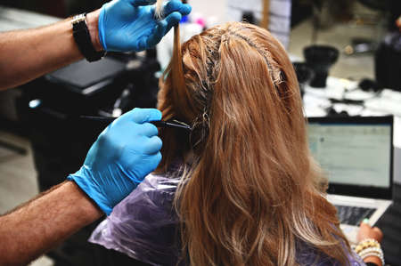 Close-up of hairdresser applying dye on hair of business woman working on laptop in beauty salonの写真素材