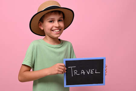 Handsome boy holding a board with travel lettering, smiling, looking at the camera. Pink background with copy spaceの写真素材
