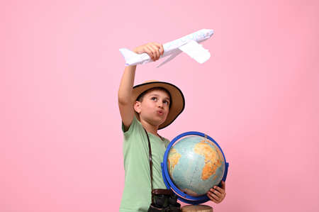 A cute schoolboy traveler holds a globe and an airplane in his hands, simulating a flight around the...