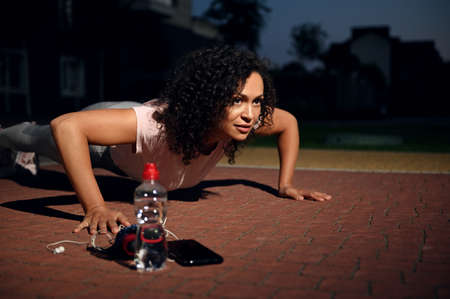 Close-up of beautiful sportswoman performing push-ups on the sportsground during evening workout....