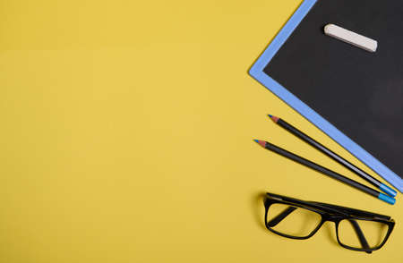 Flat lay. Chalk on a clean blackboard with copy space , eyeglasses and two pencils, isolated on yellow background with space for textの写真素材