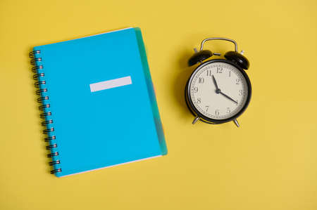 High angle view of a blue colorful notepad, organizer and an alarm clock, on yellow background with...