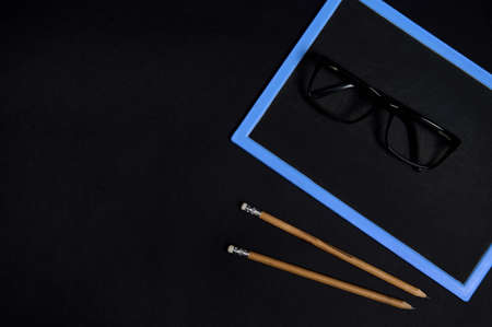 Flat lay of eyeglasses on an empty blank chalkboars and two wooden pencils on black surface background with coy spaceの写真素材