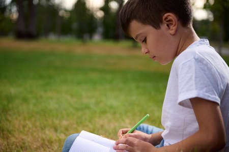 Portrait of adorable elementary aged clever student, intelligent schoolboy doing homework, solving mathematics tasks, enjoying study outdoors. Back to school, knowledge, education, erudition conceptsの写真素材