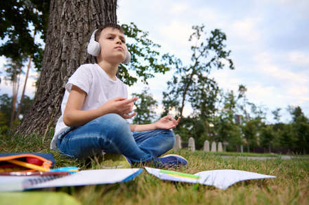 Handsome school child boy feels exhausted and tired after school and homework, sits in lotus...