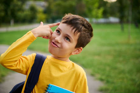 A charming joyful schoolboy holds his hand to his temple imitating a pistol, as a sign of tiredness...