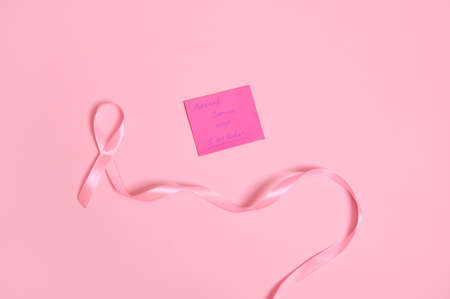 Flat lay of a long pink ribbon with endless one end, and a paper note with lettering 1 October Breast Cancer Awareness Day , isolated on pink background with space for textの写真素材