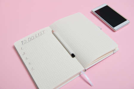 Still life. A white mobile phone lying down on pink background next to a pencil on the middle of an...