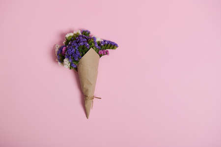 Flat lay of a floral composition of beautiful meadow flowers wrapped in wrapping craft paper tied with rope, isolated on pink background with copy space.の写真素材