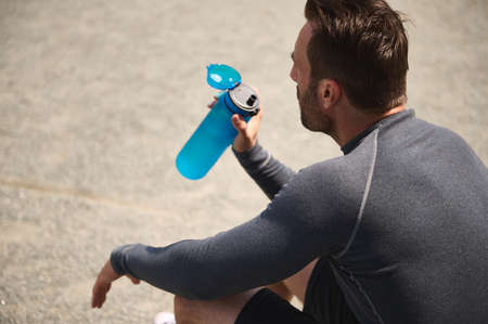 Overhead view of a mature sportsman, middle aged athlete resting and drinking water, rehydrating his...