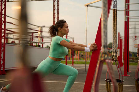 Sporty mature African American woman athlete warming up, stretching her body before and after workout session in the early morning. Sportswoman working out outdoorの写真素材