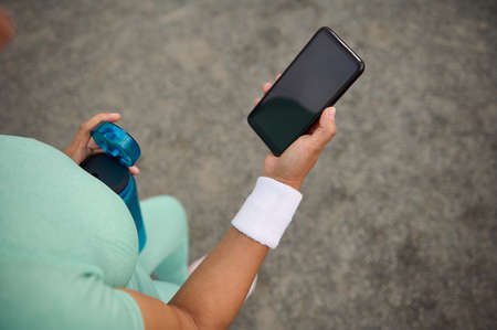 Close-up of female athlete, sports woman's hand holding a smartphone with empty blank black screen with copy space for advertisementの写真素材