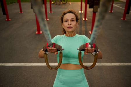 High angle view of a sporty determinate middle aged African American, mixed race woman doing arm exercises with suspension straps while performing an outdoor cross training in the sports fieldの写真素材