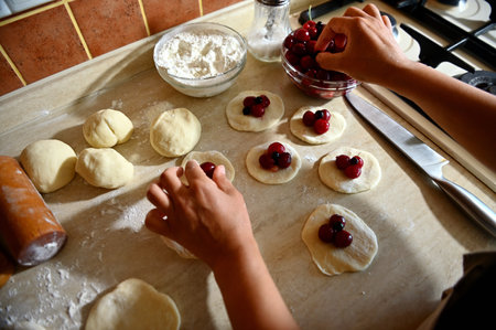 Top view of woman hands putting cherry berries on a round shape of dough, filling Ukrainian traditional dumplings. Process of cooking dumplings step by step in the kitchenの写真素材