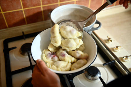 High angle view of a pastry chef taking out cooked dumplings from boiling water into a colander. Process of cooking dumplings step by step. Close-up, food background.の写真素材