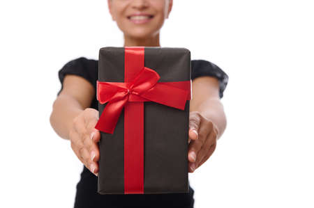 Close-up of a black gift box with red ribbon in the hands of smiling woman dressed in black isolated...
