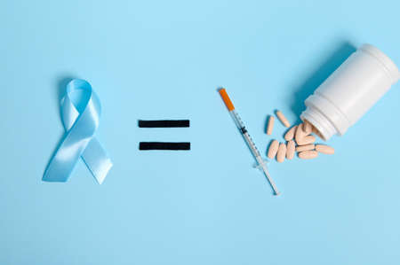 Top view of insulin syringe and pharmaceutical pills scattered from container on blue background, equal sign and blue ribbon, symbol of World Diabetes Awareness Day. Copy space for medical advertisingの写真素材