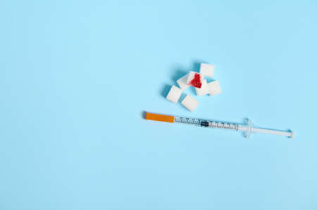Flat lay of insulin syringe and pure refined white sugar cubes with blood drop isolated over colored blue background with copy space for medical ad. World diabetes day awareness concept, 14 Novemberの写真素材