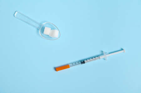 White sugar cubes on a transparent measuring spoon and insulin syringe on colored blue background with copy space for medical concept advertising. World diabetes day awareness concept, 14 Novemberの写真素材