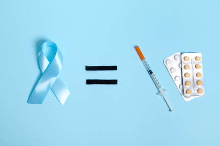 Flat lay of insulin syringe and blister with medical pills on blue background, equal sign and blue ribbon, symbol of World Diabetes Awareness Day, 14 November. Copy space for medical advertisingの写真素材