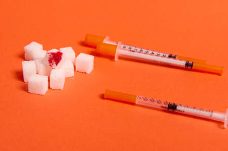 Pure refined white sugar cubes with blood drop and insulin syringes lying on orange background with copy space for World Diabetes Day medical advertisement. World diabetes awareness day, 14 Novemberの写真素材