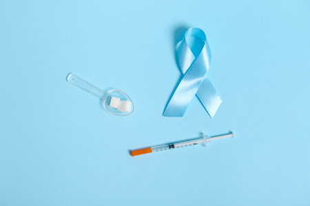 Top view of insulin syringe, sugar cubes on measuring spoon and blue ribbon, symbol of World Diabetes Awareness Day 14 November. Medical concept for advertisement on blue background with copy spaceの写真素材