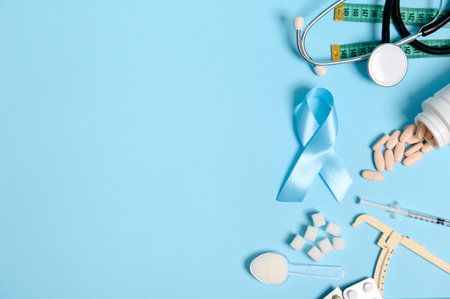 Scattered pharmaceutical pills, insulin syringe, stethoscope, caliper, measuring tape, refined white sugar and blue awareness ribbon, symbol of World Diabetes Day, colored background with copy space.の写真素材